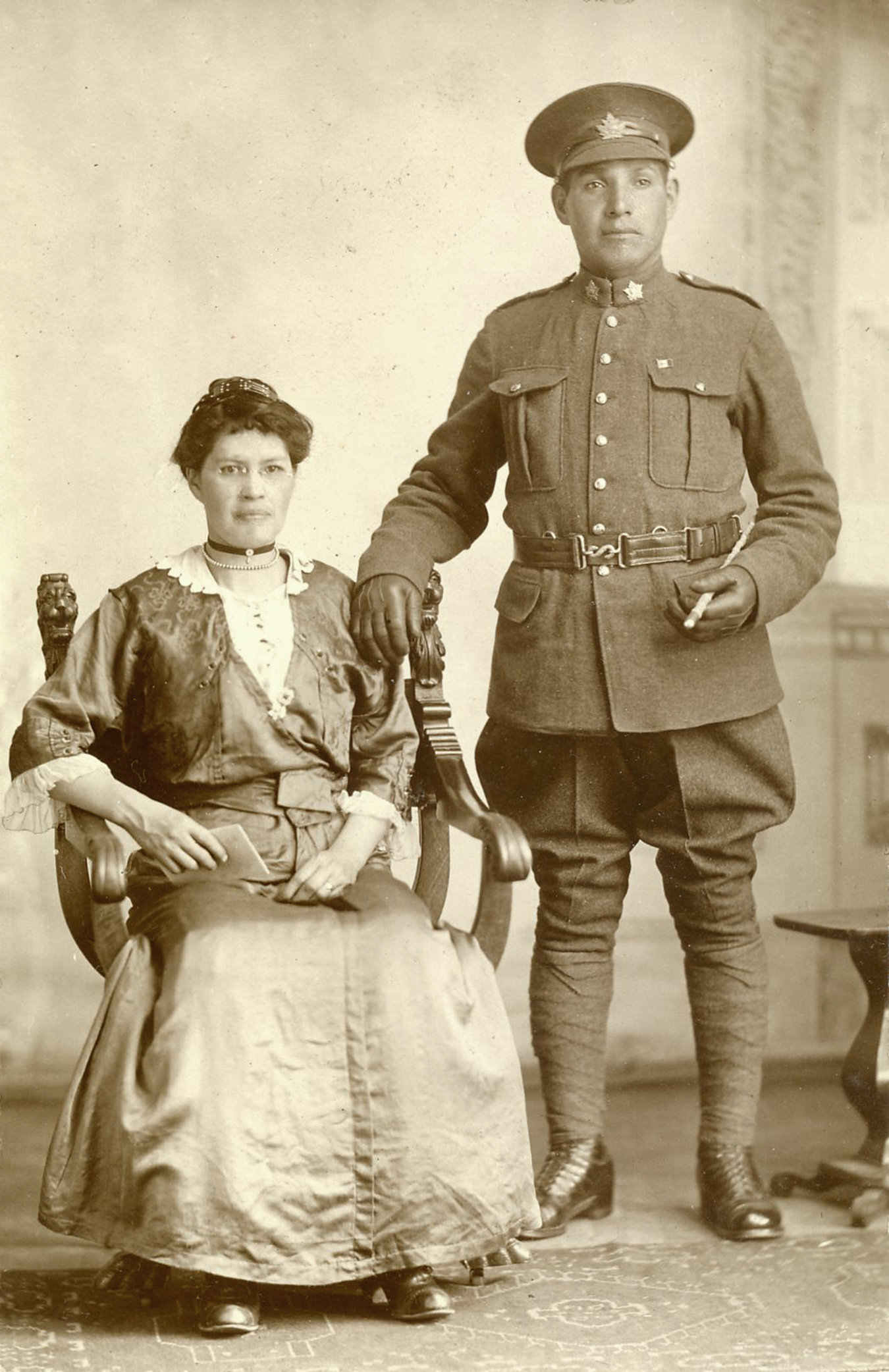 Black and white photograph of Wilfred Lickers, in uniform standing next to his and his first wife, Eva, who is seated in a chair